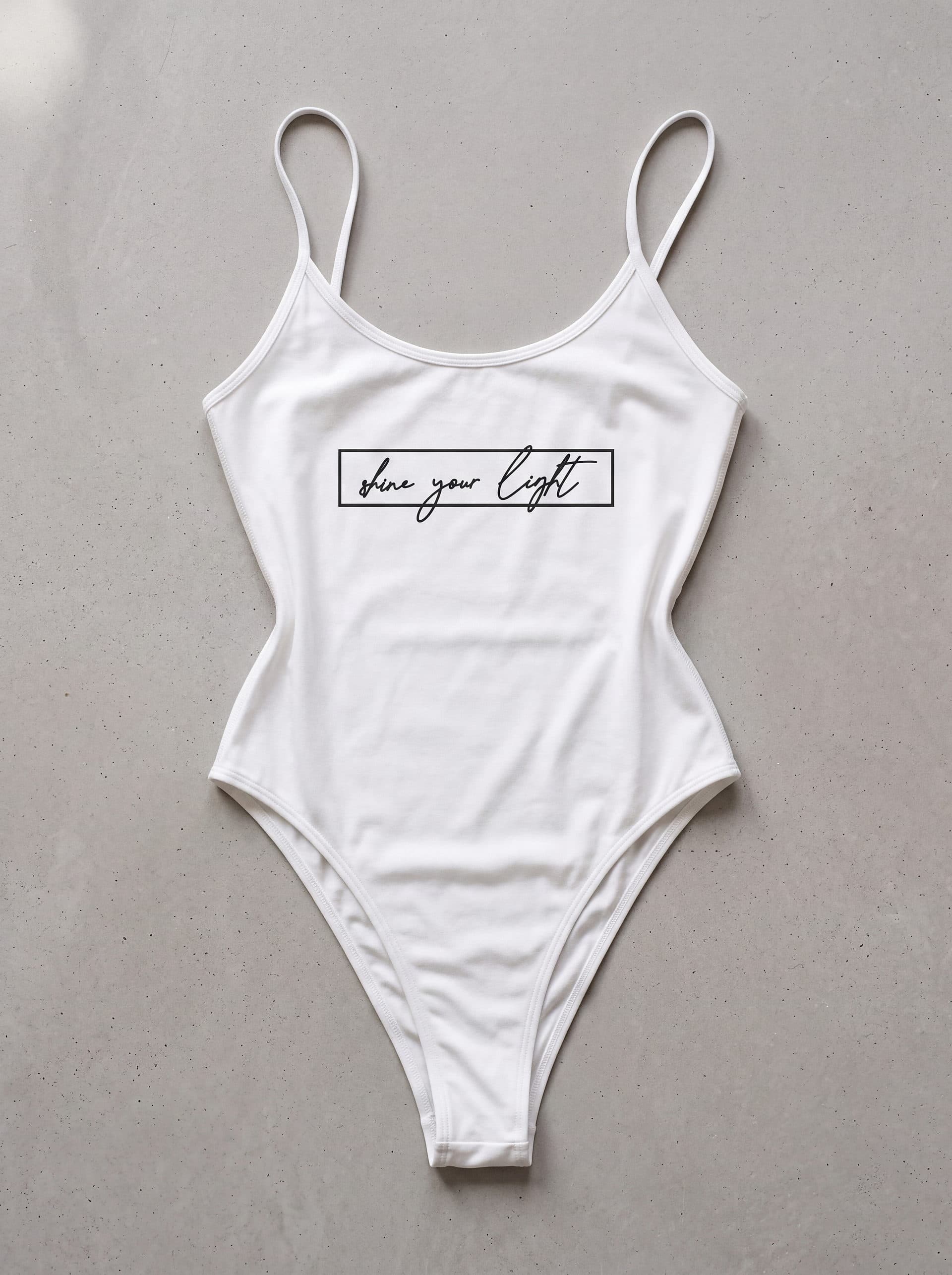 Body tirantes Shine Your Ligth, en color blanco, prenda sola sobre fondo de cemento