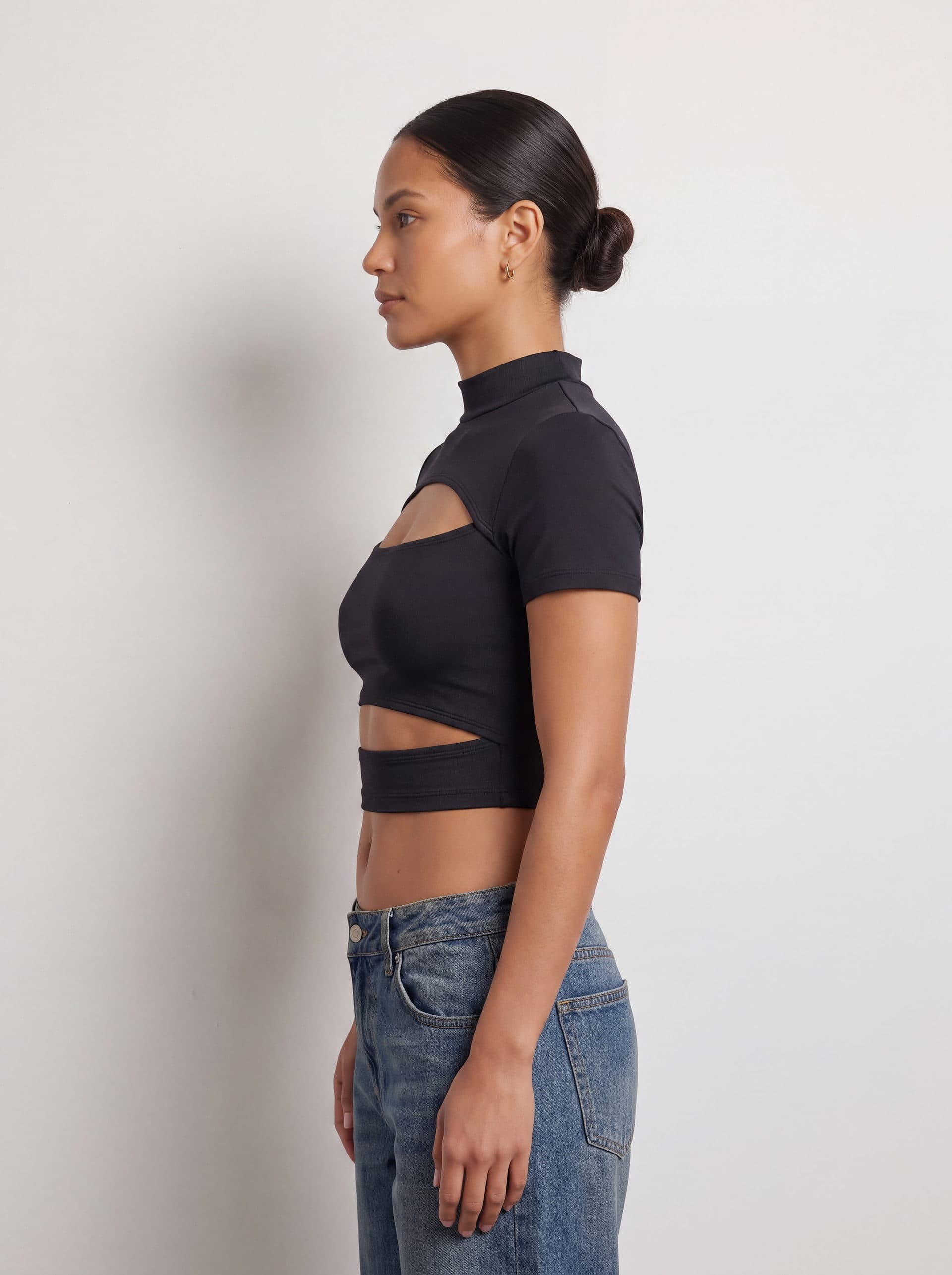 Crop top con doble abertura, en color negro, de perfil en modelo