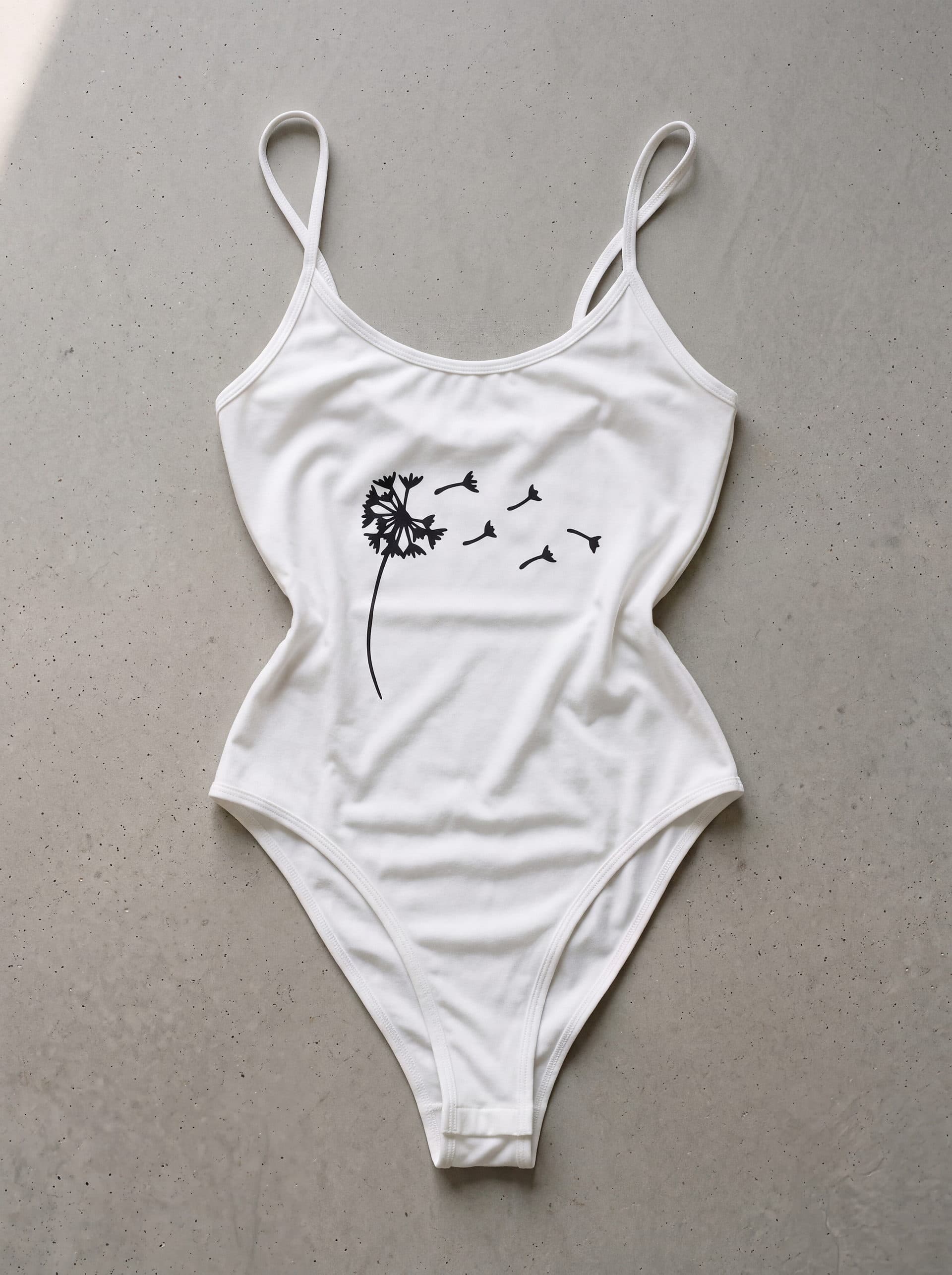 Body tirantes Diente de león, en color blanco, prenda sola sobre fondo de cemento