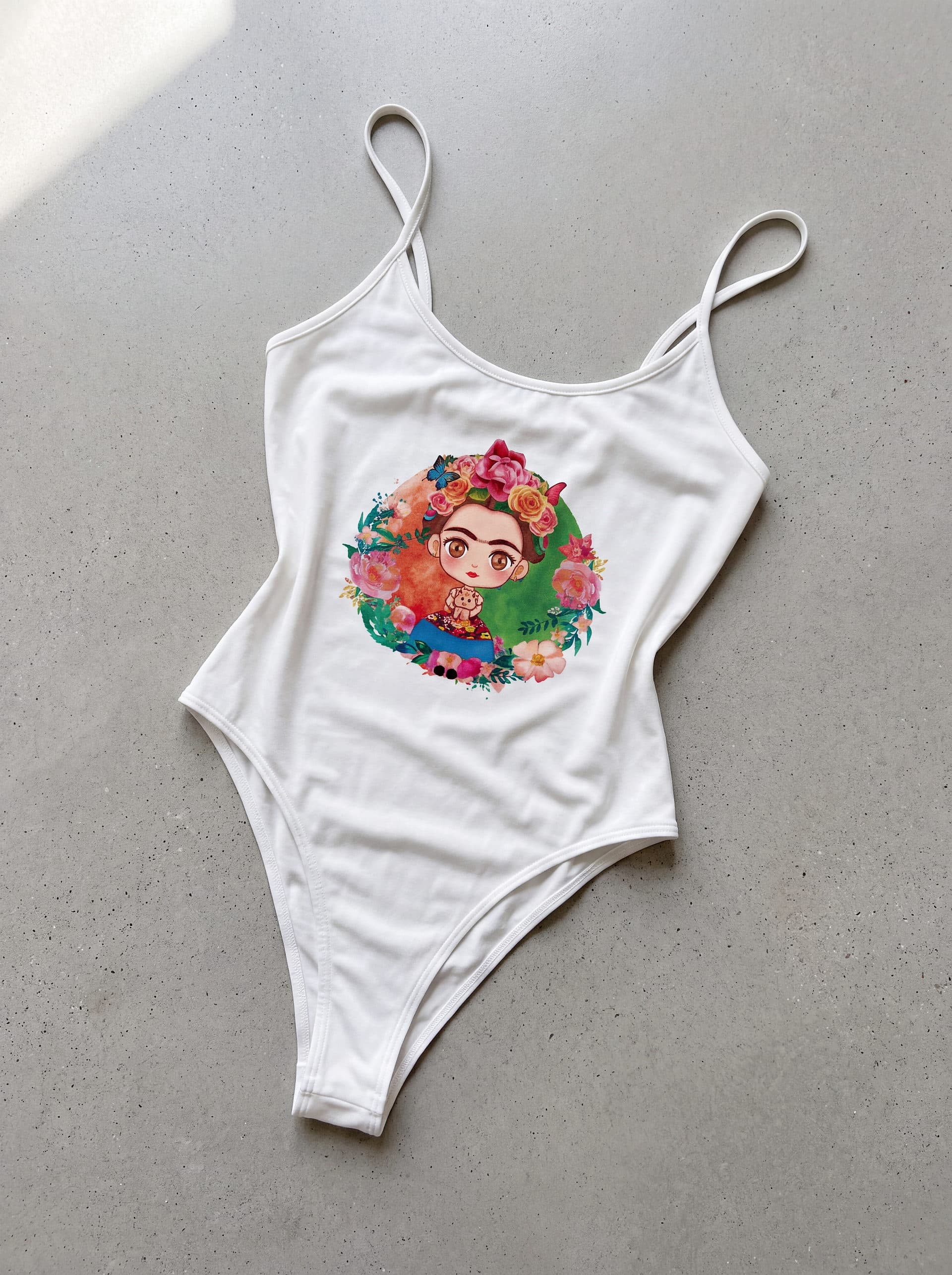 Body tirantes Frida Kahlo Luna, en color blanco, prenda sola sobre fondo de cemento