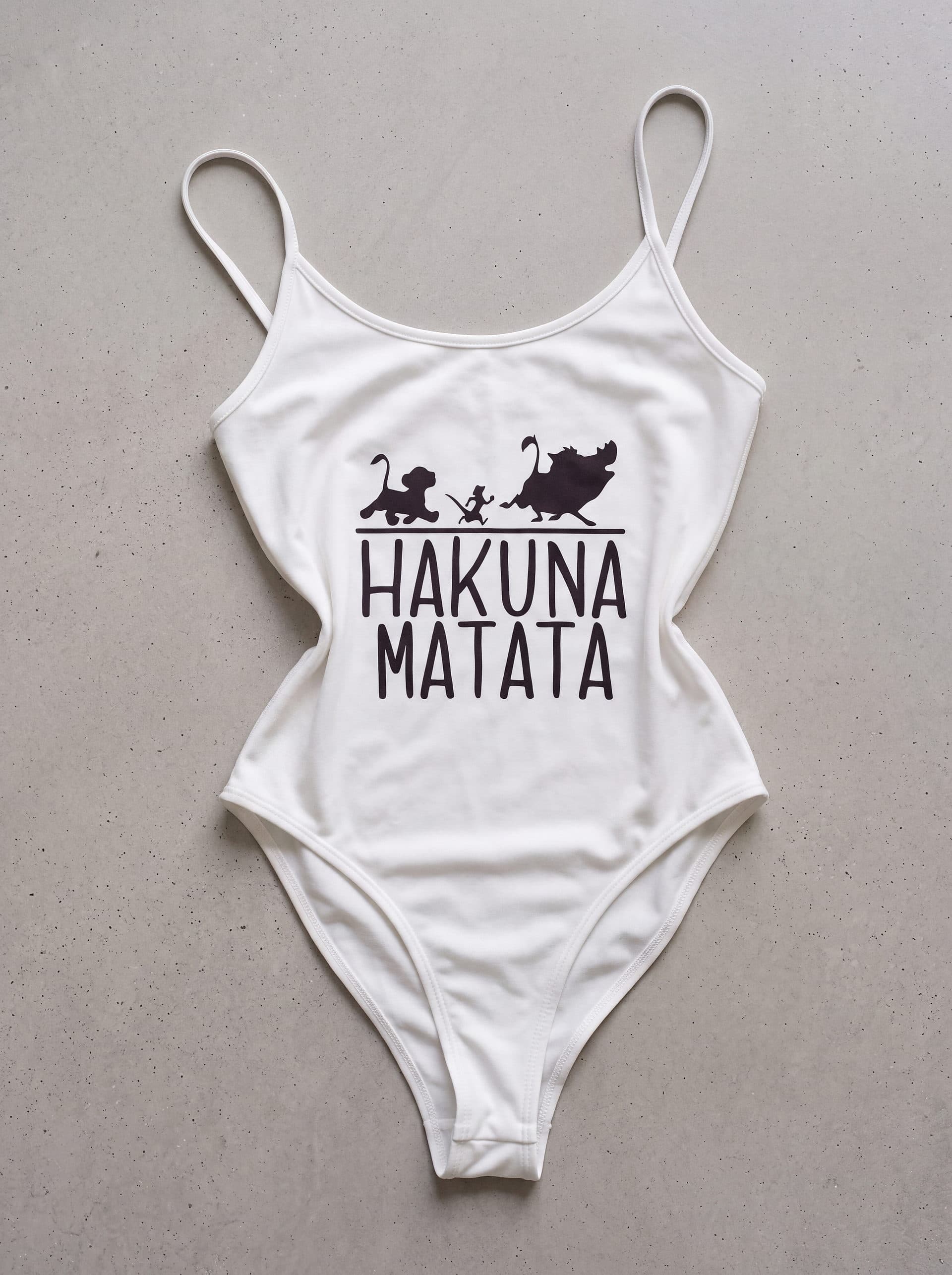 Body tirantes Hakuna Matata, en color blanco, prenda sola sobre fondo de cemento