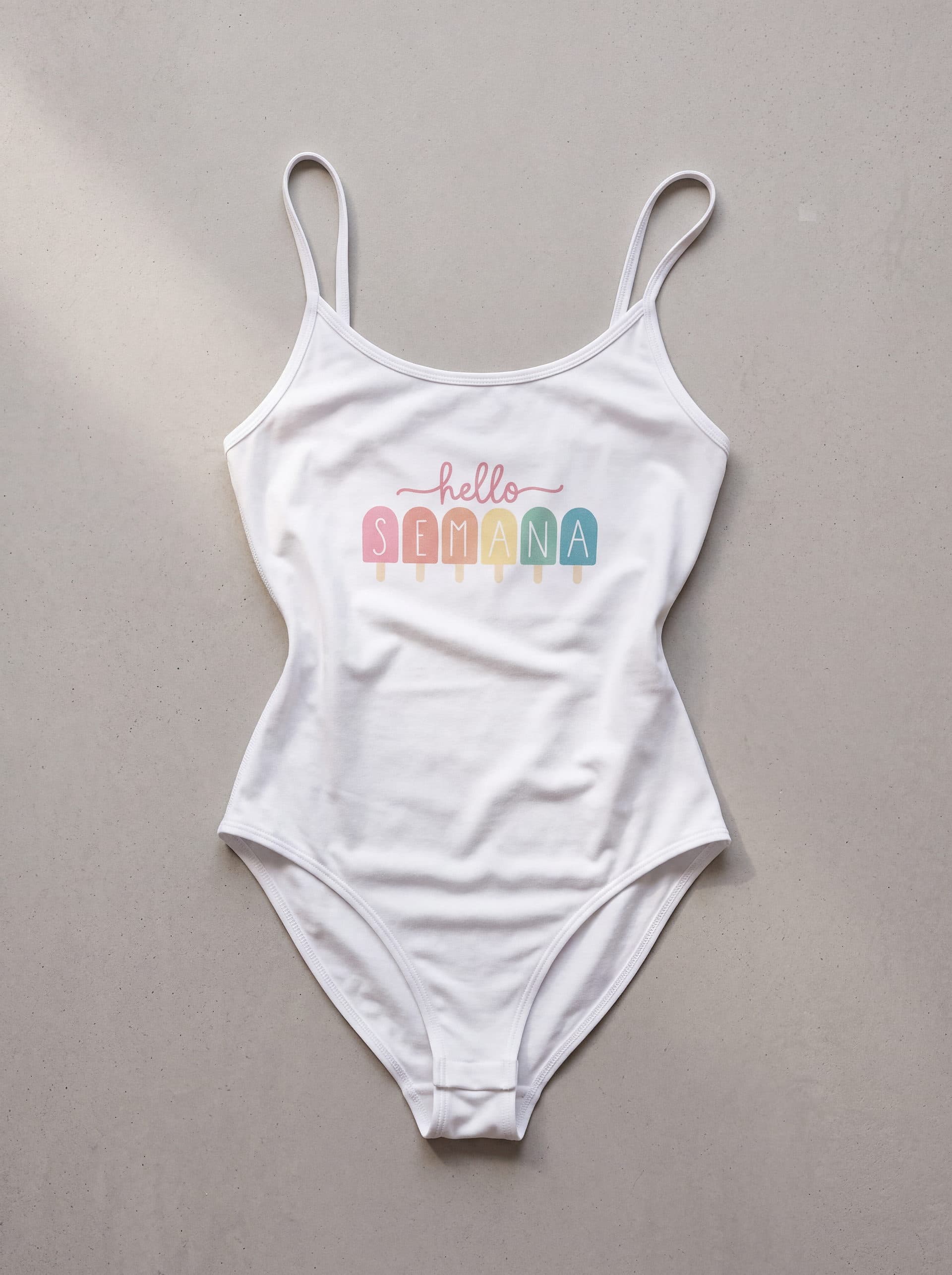 Body tirantes Hello Semana, en color blanco, prenda sola sobre fondo de cemento