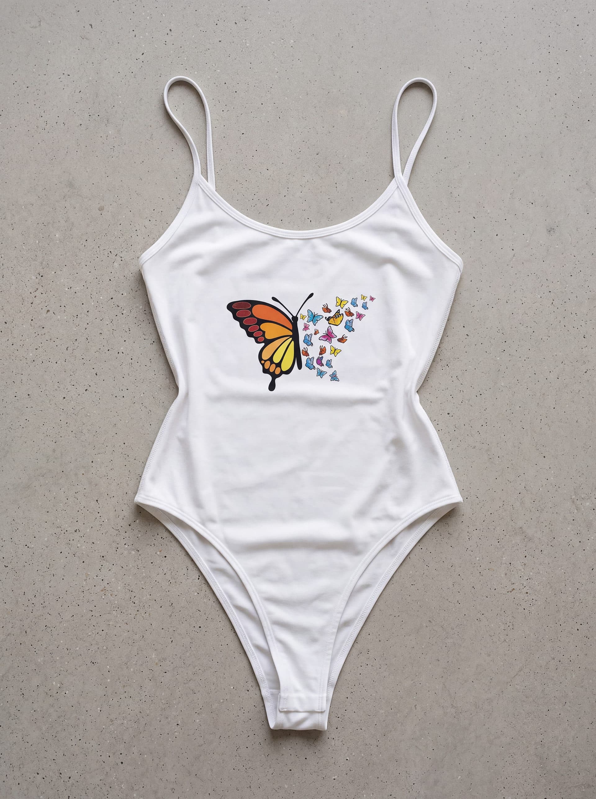 Body tirantes Mariposa con maripositas, en color blanco, prenda sola sobre fondo de cemento